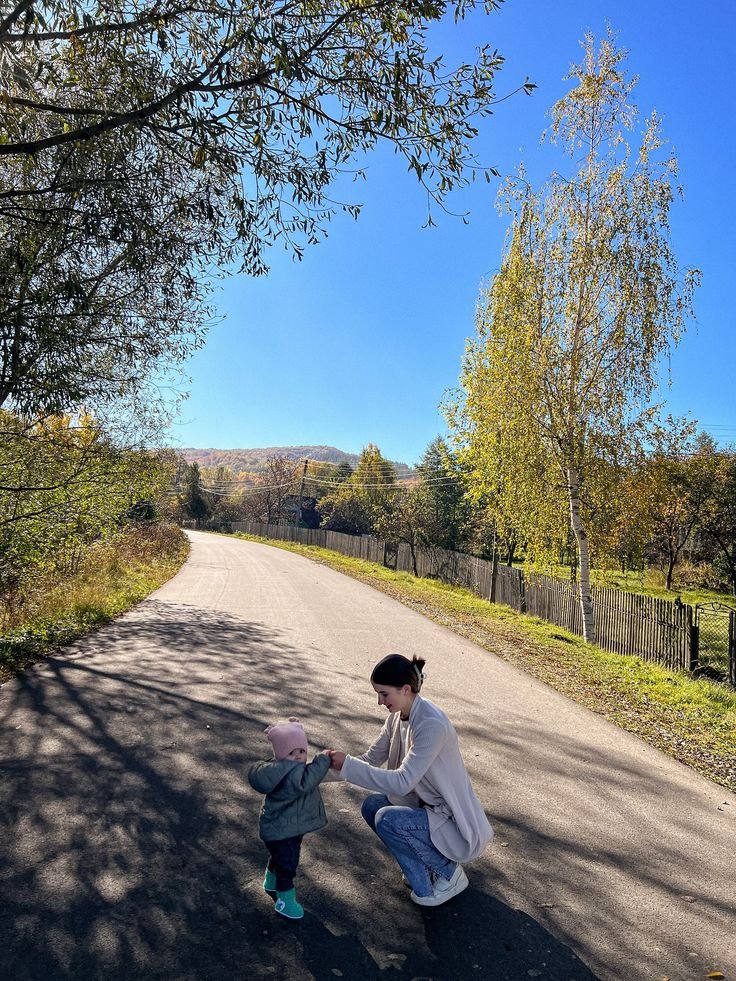 This may contain: a woman kneeling down next to a small child on a road with trees in the background