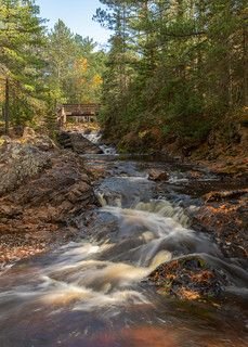 This may contain: a river running through a forest filled with lots of rocks and trees next to a bridge