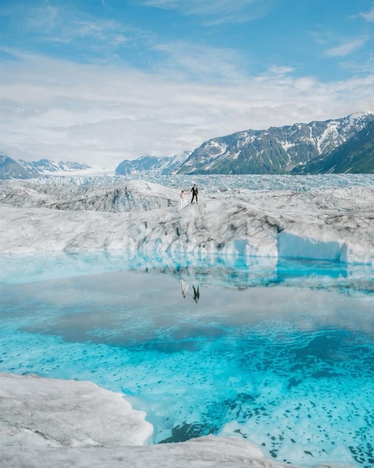 This may contain: two people are standing on an ice floet in the middle of mountains and water