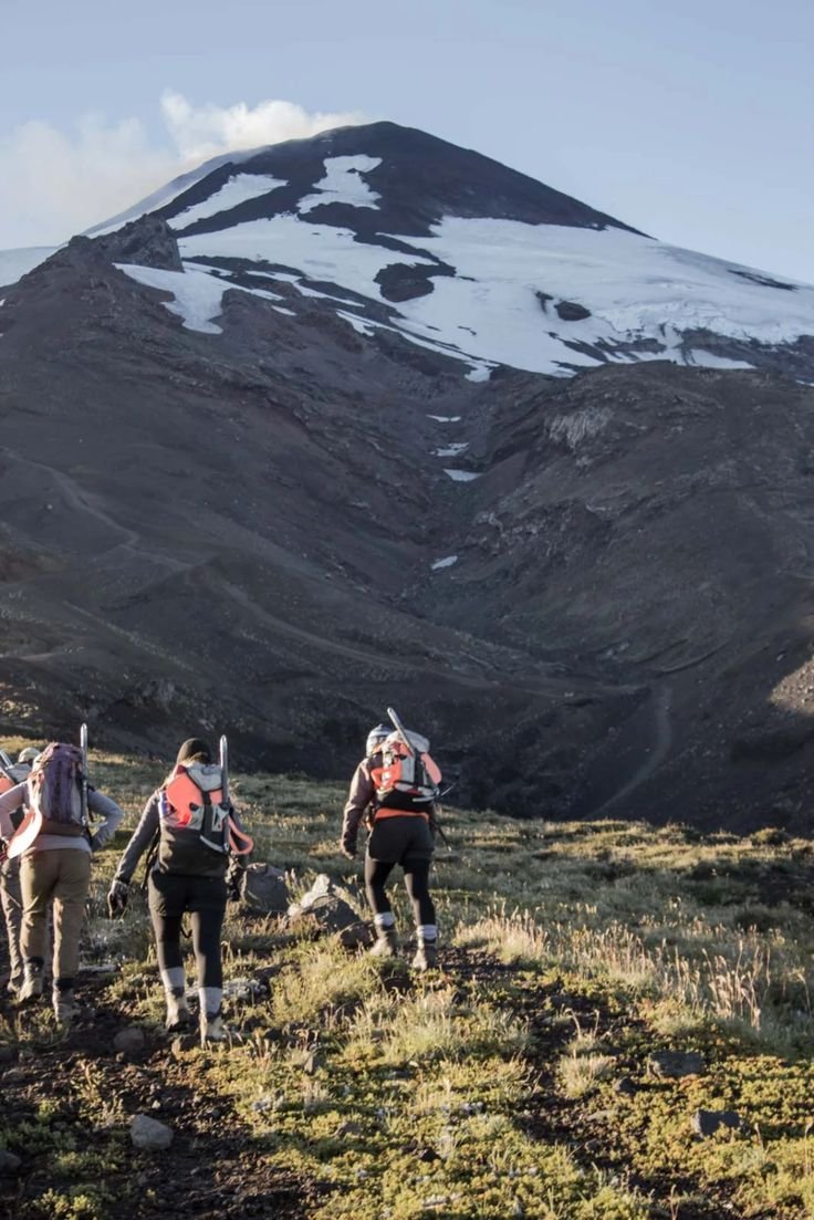 This may contain: three people hiking up a hill with a mountain in the background and snow on the top