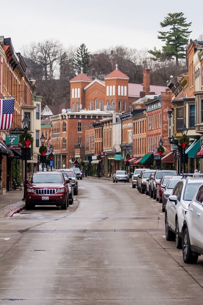 This may contain: cars are parked on the street in front of shops and buildings with an american flag hanging from the roof