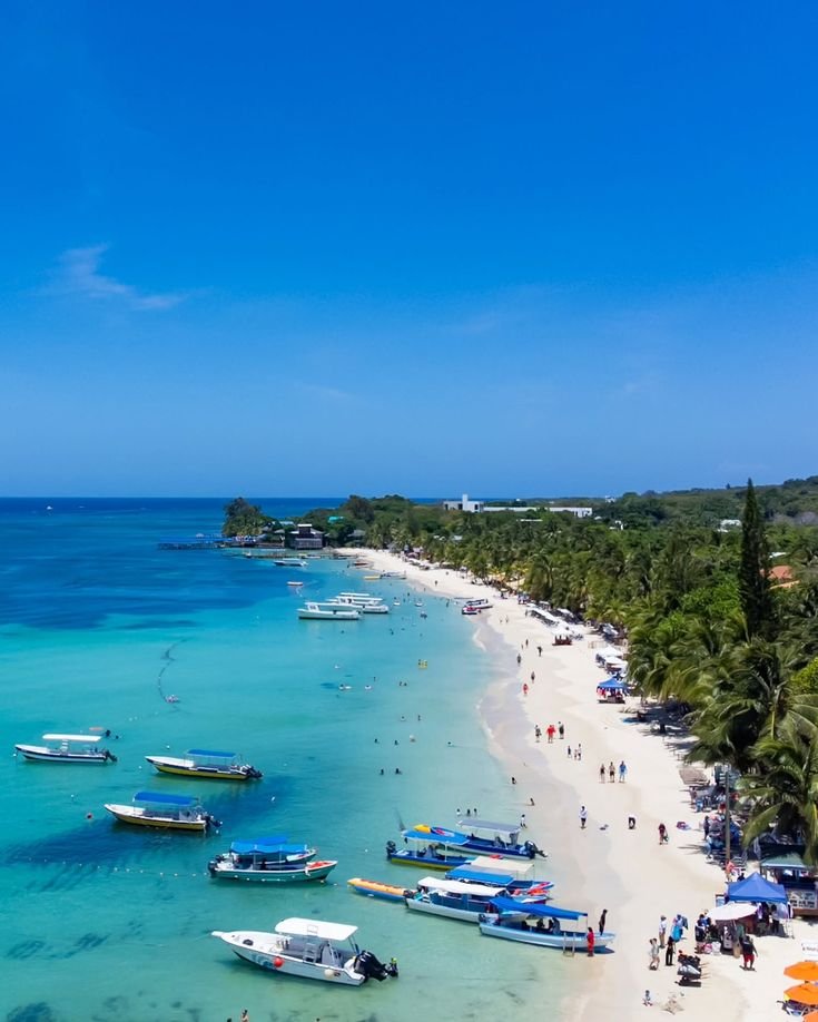 This may contain: boats are parked on the beach as people walk along it and swim in the water