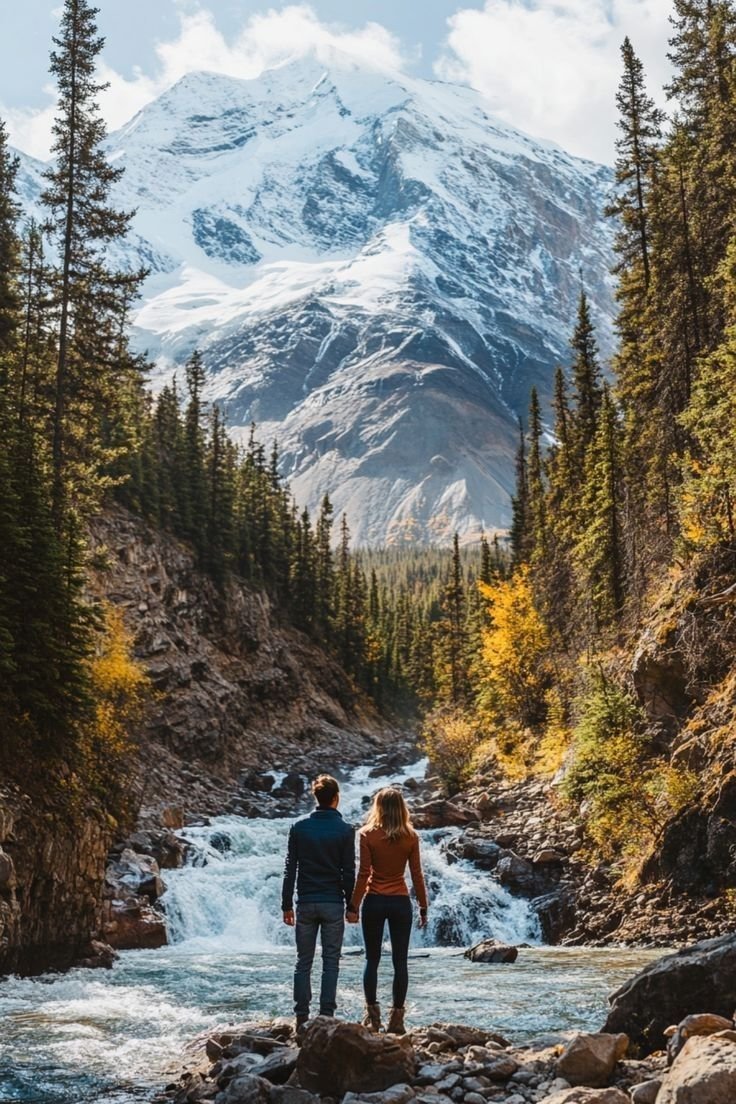 This may contain: a man and woman standing on rocks in front of a river with mountains in the background
