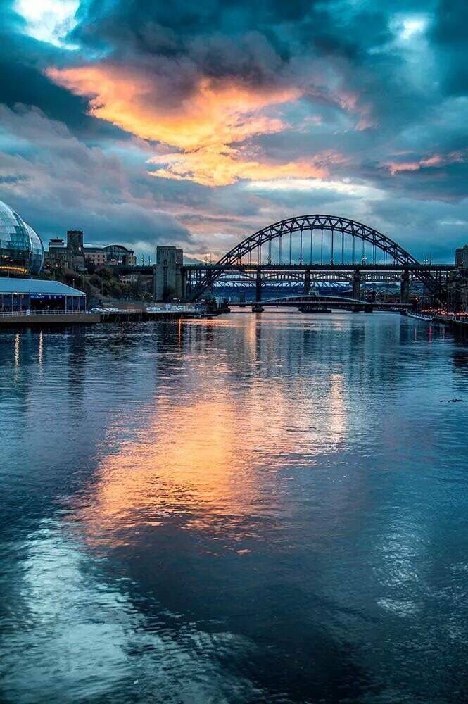 This may contain: the sun is setting behind a bridge and some clouds are in the sky above it