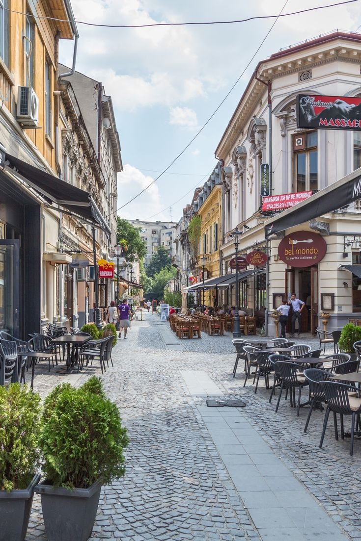 This may contain: a cobblestone street with tables and chairs in the middle, surrounded by buildings