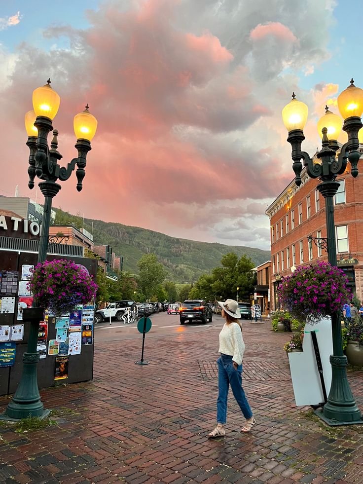 This may contain: a woman walking down the street in front of some lamps and buildings with flowers on them