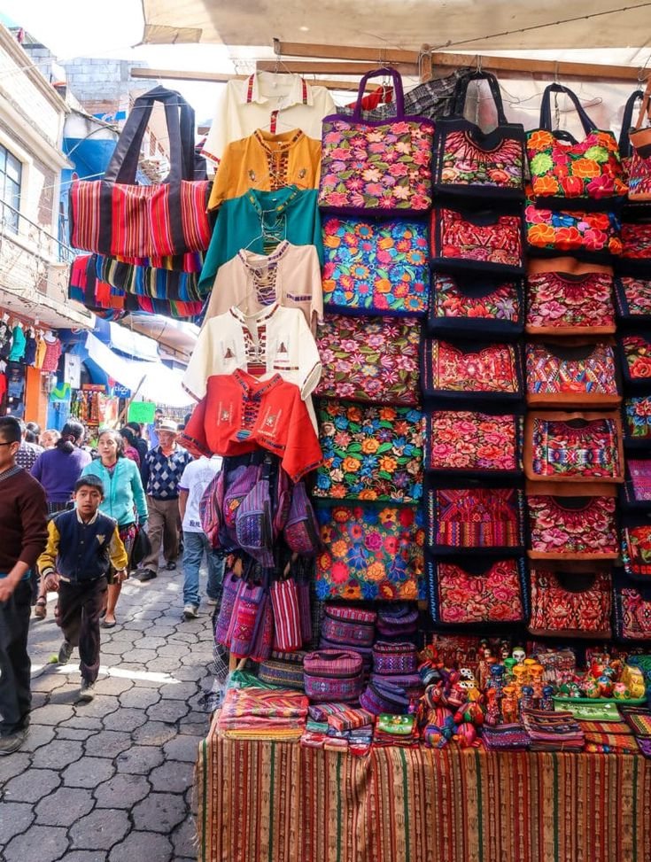 This may contain: many bags and t - shirts are on display at an outdoor market