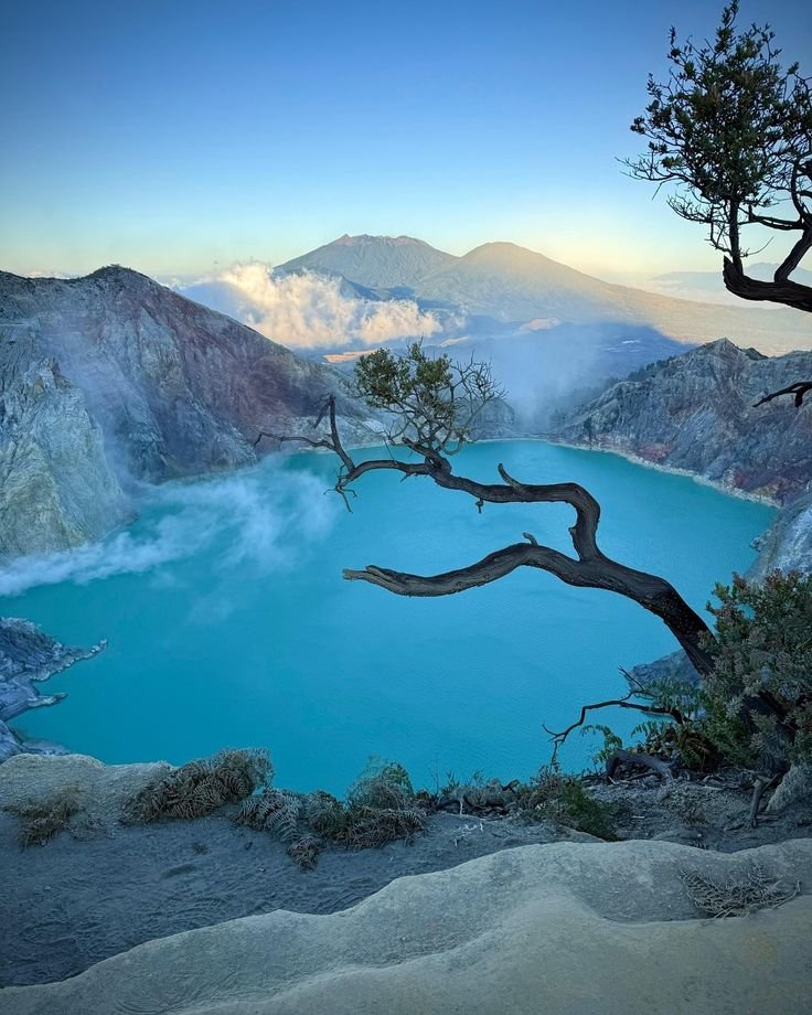 This may contain: a blue lake surrounded by mountains with trees in the foreground and water on the other side