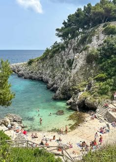 This may contain: people are on the beach and in the water near some cliffs with stairs leading up to them