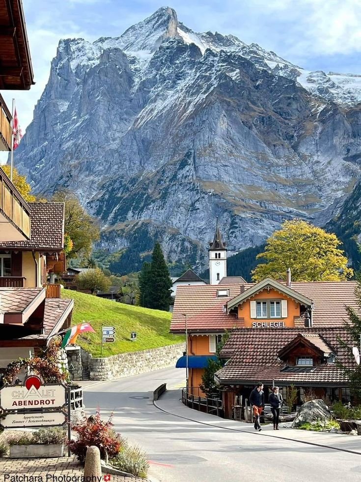 This may contain: people are walking down the street in front of some buildings with mountains in the background