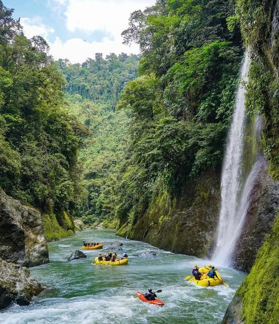This may contain: several people are rafting down a river in front of a waterfall