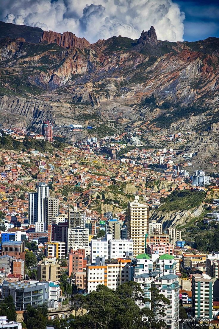 This may contain: a city with mountains in the background and clouds above it, as seen from an overlook point