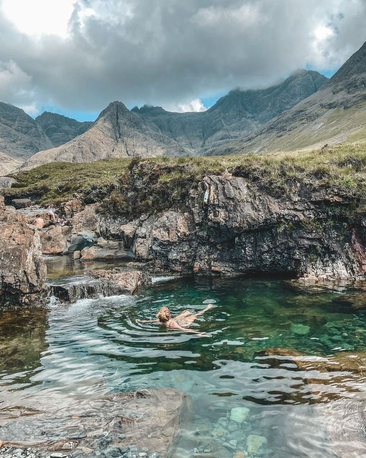 This may contain: a person swimming in the water near mountains