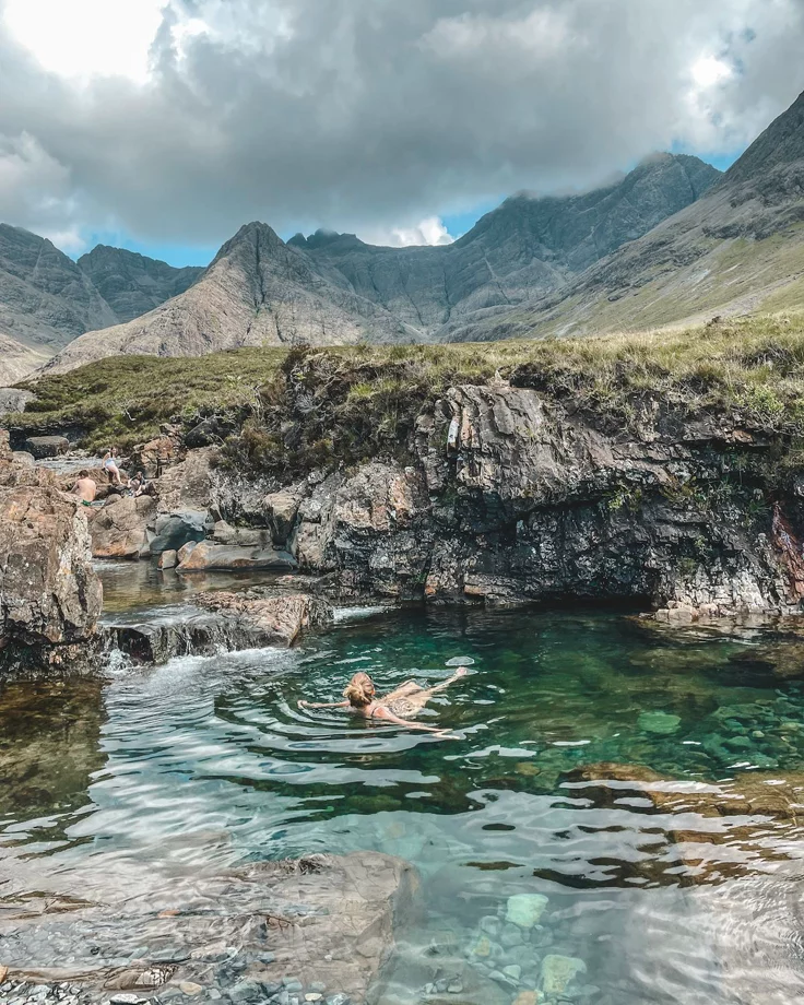 This may contain: a person swimming in the water near mountains