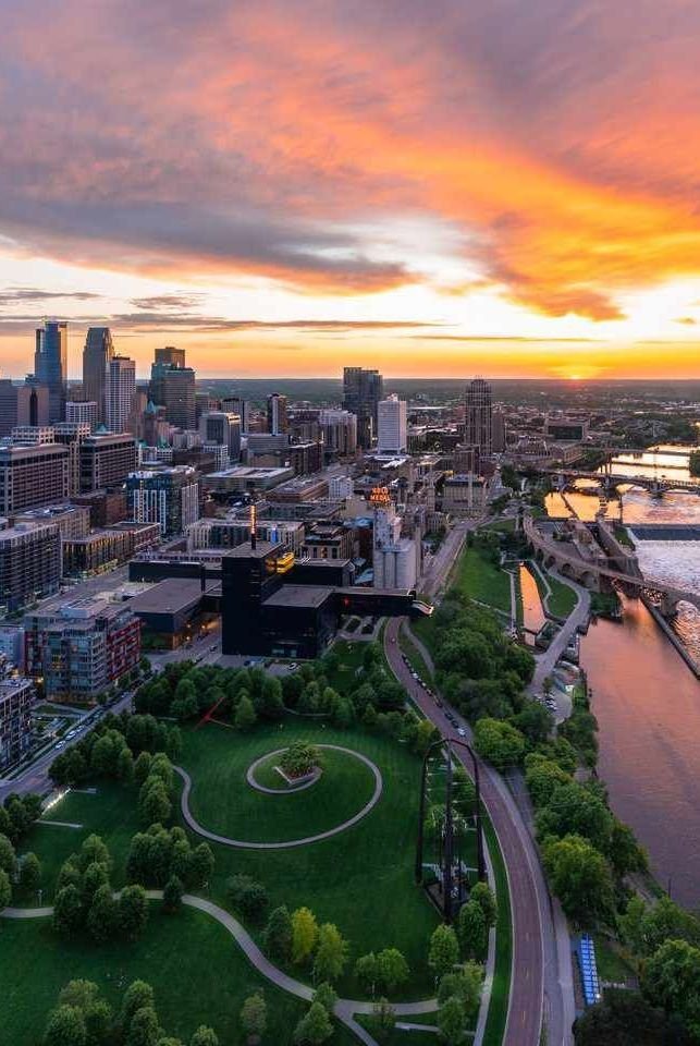 This may contain: an aerial view of a city at sunset with the sun setting in the distance and river running through it