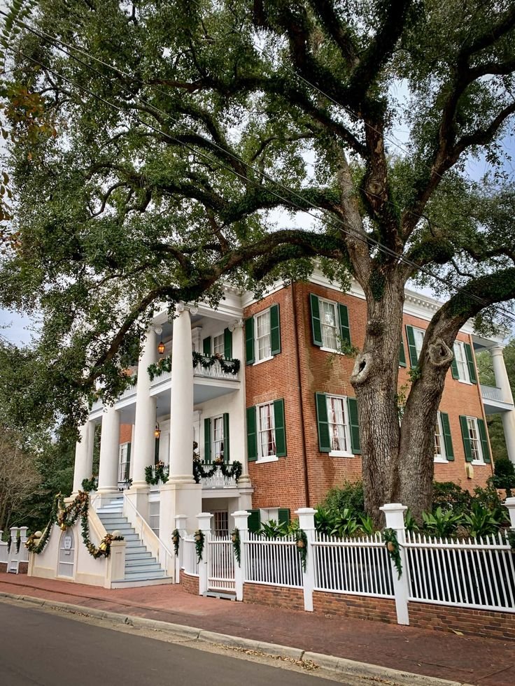 This may contain: a large red brick building with white pillars and green shutters on the front porch