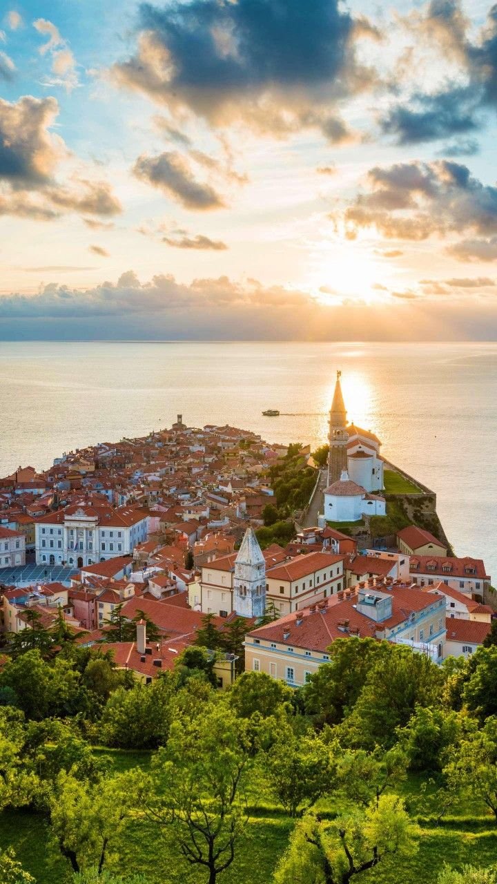 This may contain: the sun is setting over a small town on top of a hill overlooking the ocean