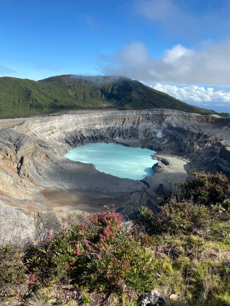 This may contain: a large crater in the middle of a mountain range with blue water and green vegetation