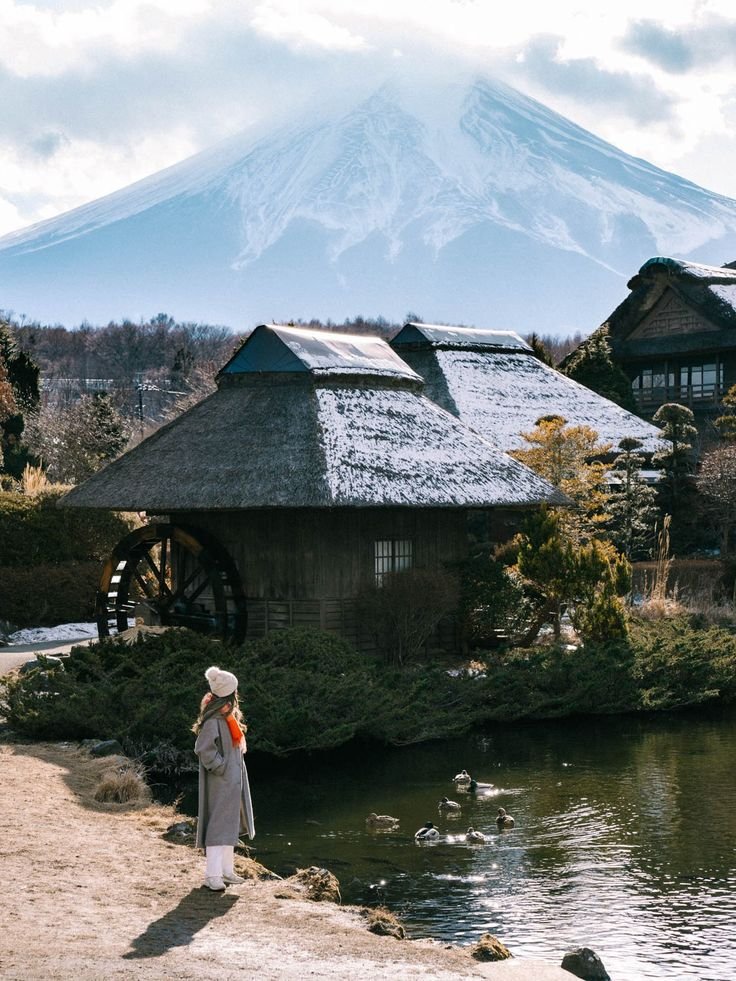 This may contain: a woman standing in front of a lake with a mountain in the background