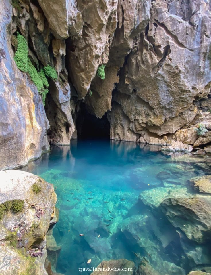 This may contain: the blue pool is surrounded by large rocks and green mossy trees in the background