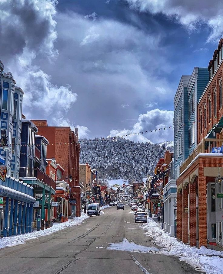 This may contain: a street lined with shops and buildings under a cloudy sky in the town of steamboat, colorado