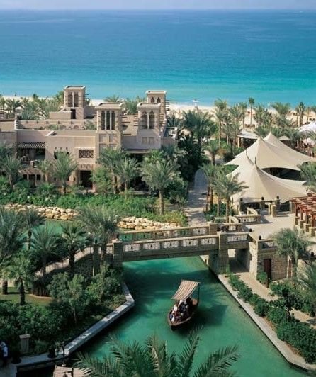 This may contain: an aerial view of a resort with a boat in the water and palm trees surrounding it