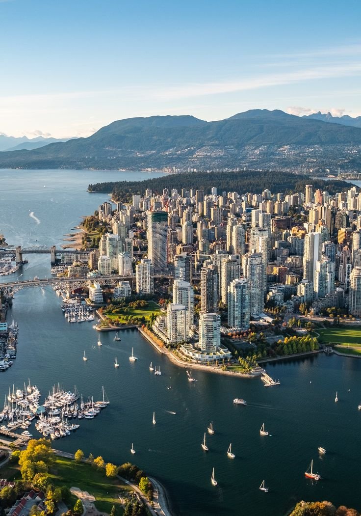 This may contain: an aerial view of a city and harbor with sailboats in the water, surrounded by mountains