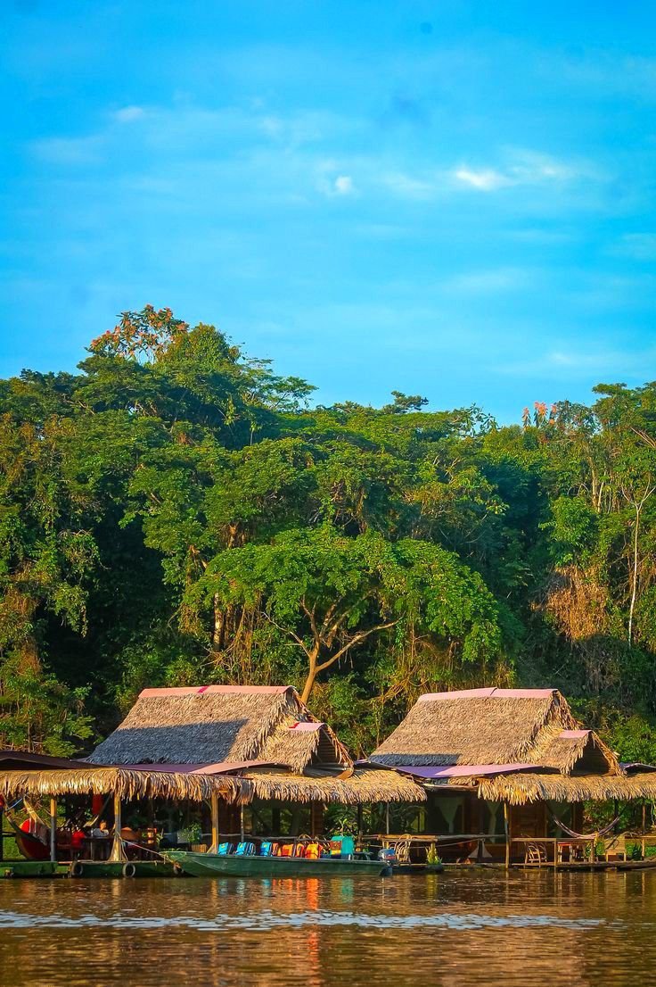 This may contain: some huts are sitting on the edge of a body of water with trees in the background