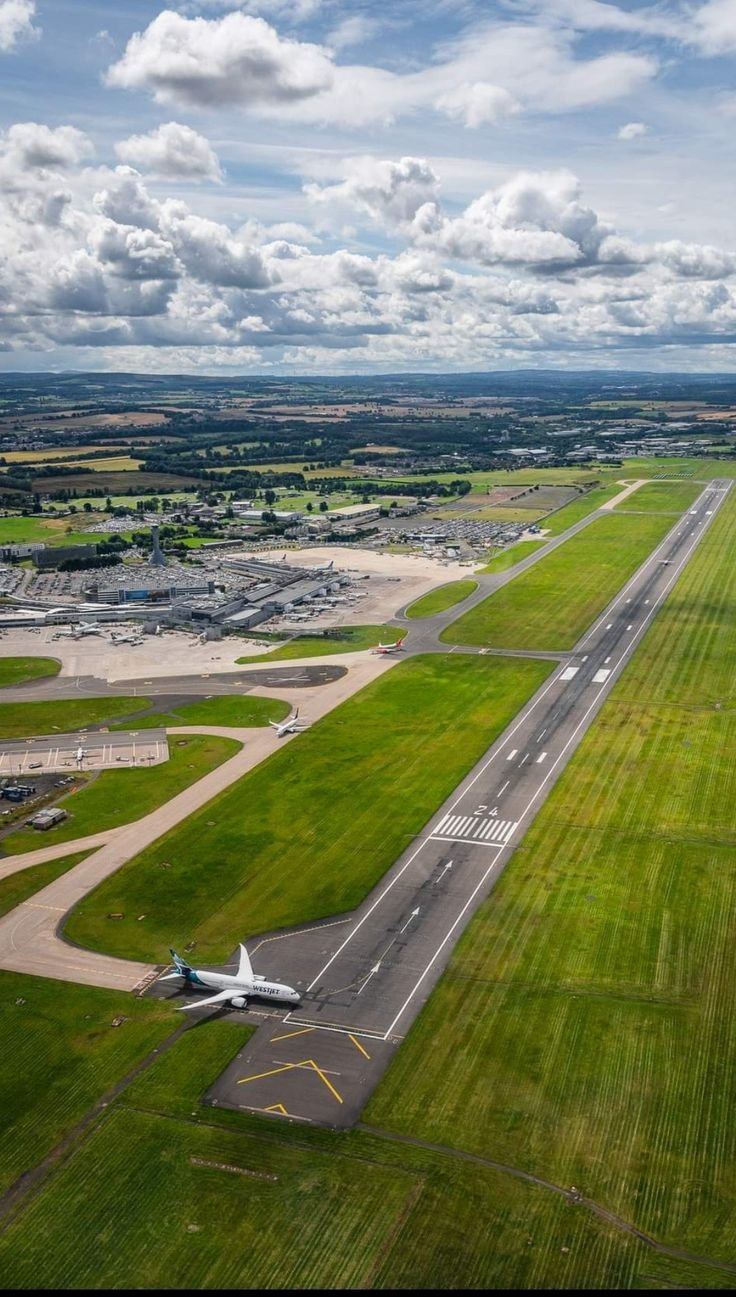 This may contain: an airplane is parked on the runway in front of some buildings and green grass with clouds