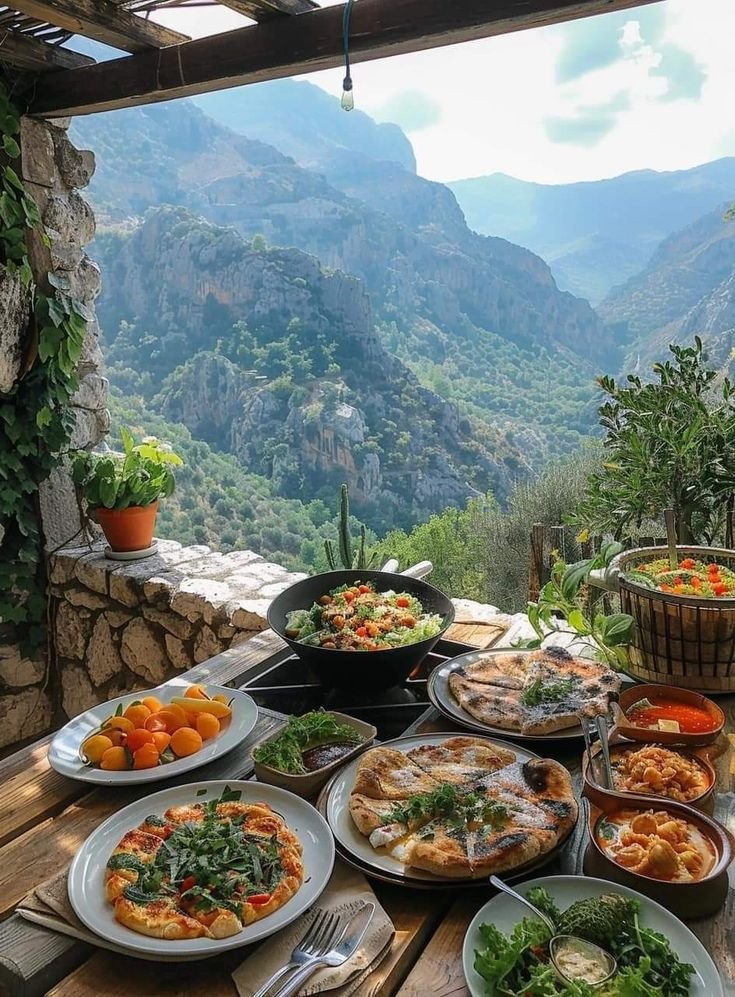 This may contain: a table full of food with mountains in the background