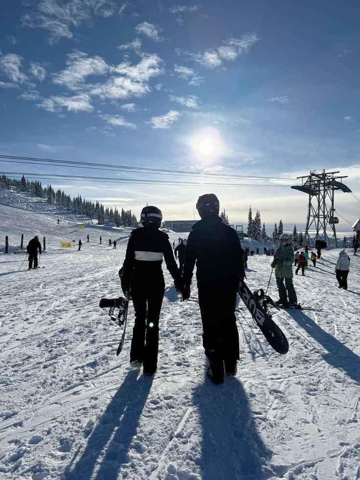 This may contain: two people standing in the snow with skis on their shoulders and one holding hands