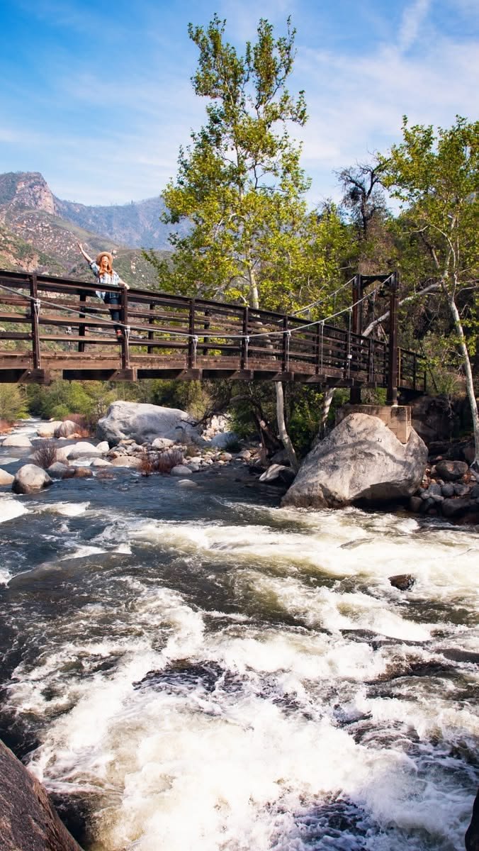 This may contain: a person standing on a bridge over a river with rapids and rocks in the foreground