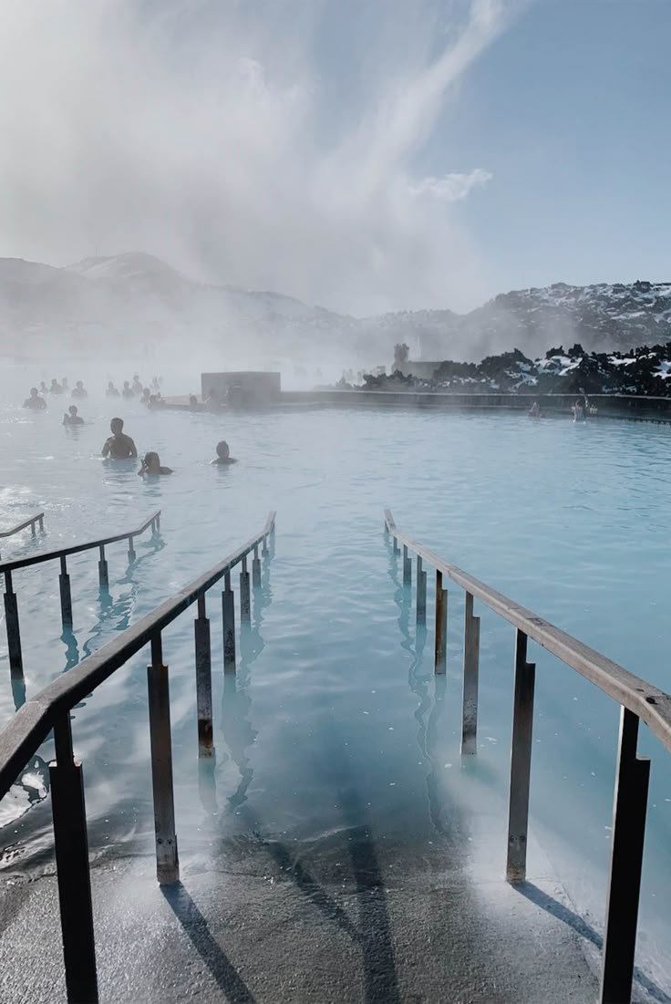 This may contain: people are swimming in the blue lagoon on a sunny day with steam rising from the water