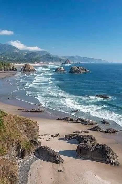 This may contain: the beach is next to an ocean and some rocks in the sand with mountains in the background