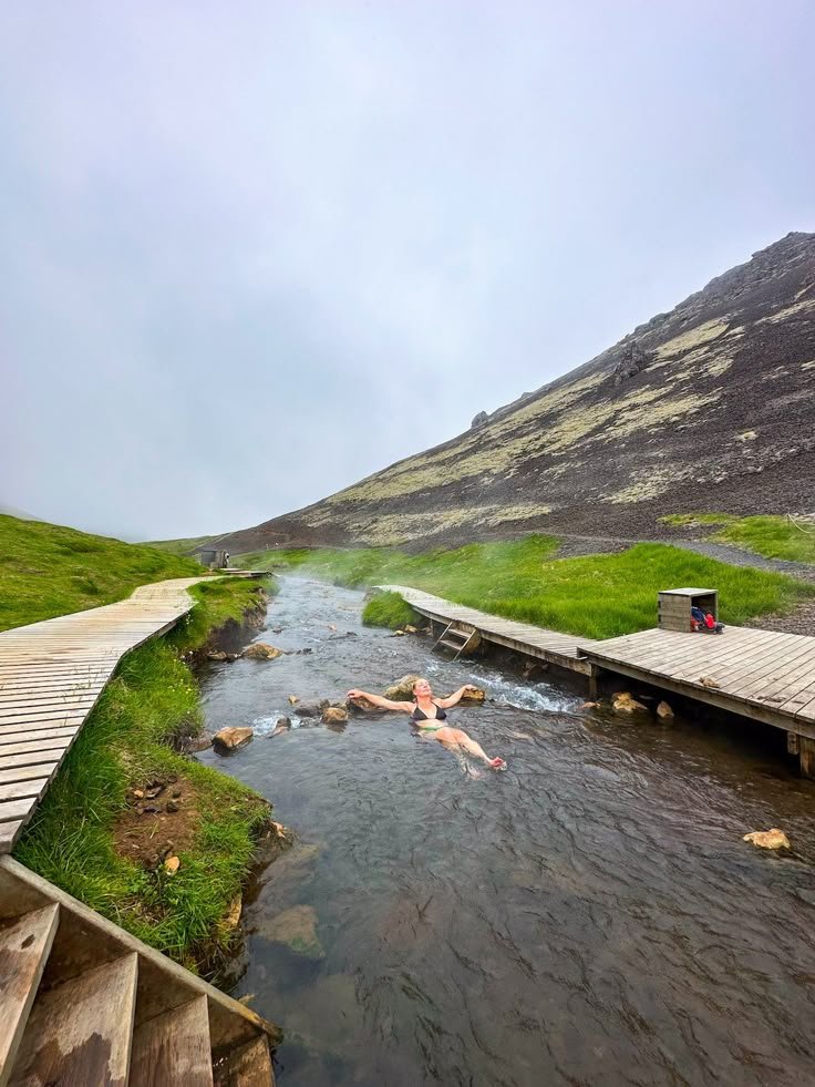 This may contain: people are swimming in the water near wooden steps and stairs that lead up to a hill