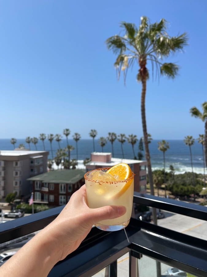 This may contain: a person holding up a glass with an orange slice in it on top of a balcony