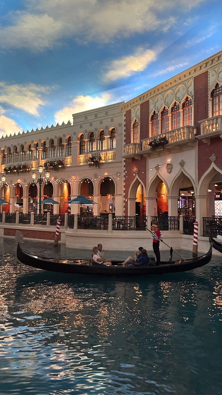 This may contain: a gondola in the middle of a river with people on it and buildings around