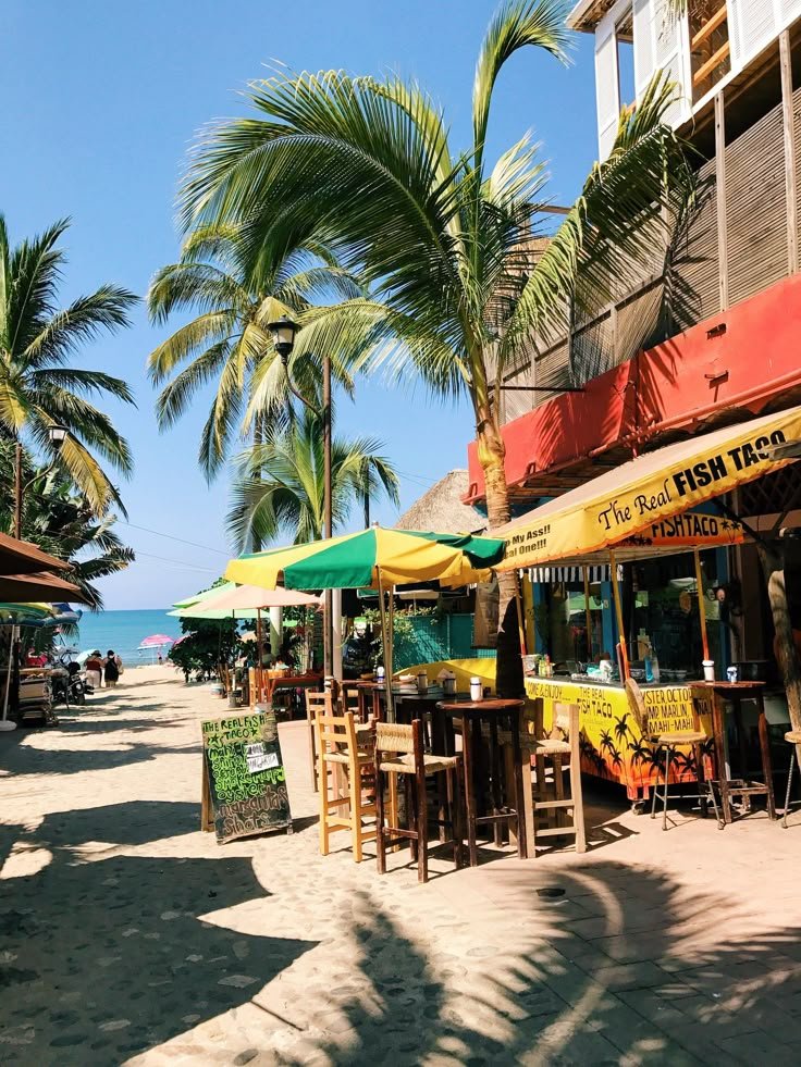 This may contain: there are many tables and chairs under umbrellas at the beach side restaurant on the sand