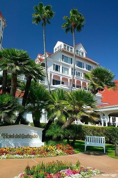 This may contain: a large white building with palm trees and flowers around it