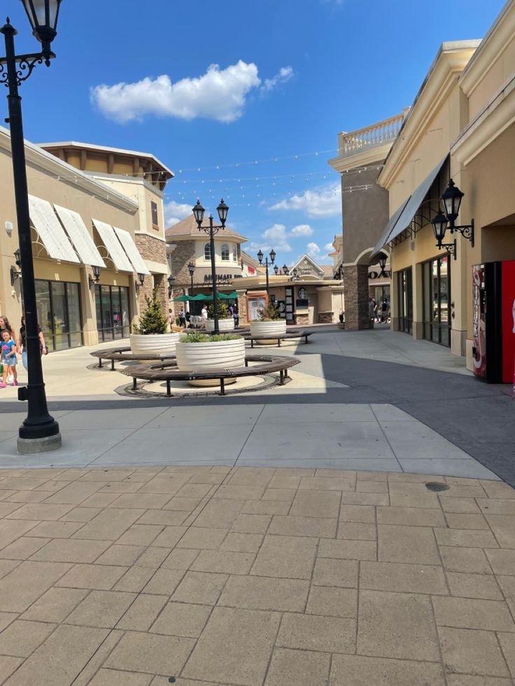 This may contain: an empty shopping center with benches and lamps on the side walk in front of shops