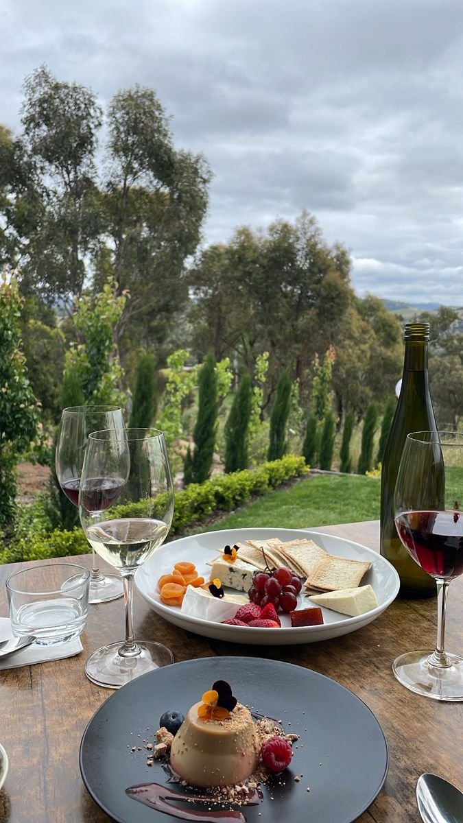 This may contain: two plates with desserts and wine glasses on a table in front of some trees