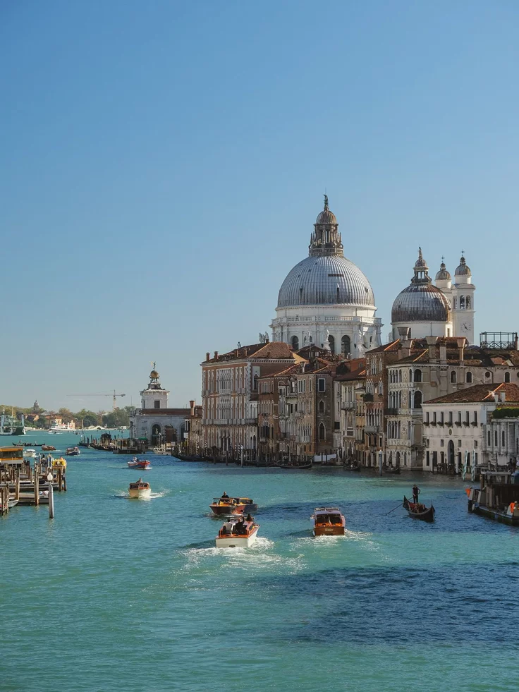 This may contain: several boats are traveling down the water in front of buildings and domed domes on top of them