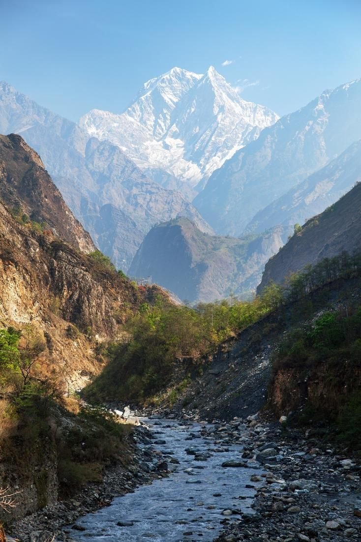 This may contain: a river running through a valley with mountains in the background