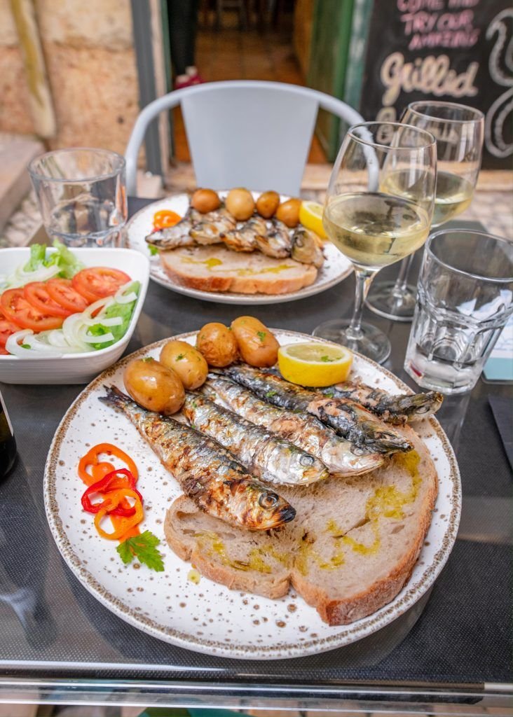 This may contain: there is a plate with fish and vegetables on it next to some glasses of wine