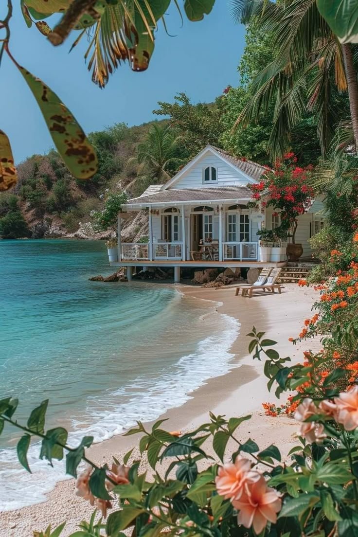 This may contain: a white house sitting on top of a sandy beach next to the ocean with lots of flowers
