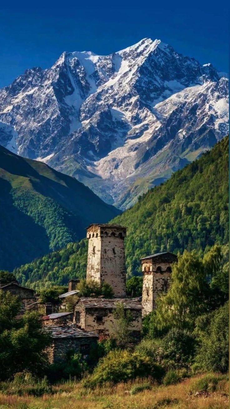 This may contain: the mountains are covered in snow and there is an old building on the hill side