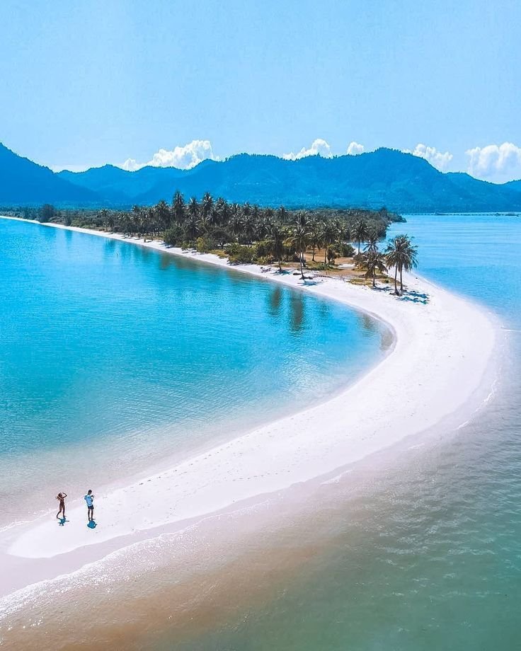 This may contain: two people are walking on the beach in front of an island with white sand and palm trees