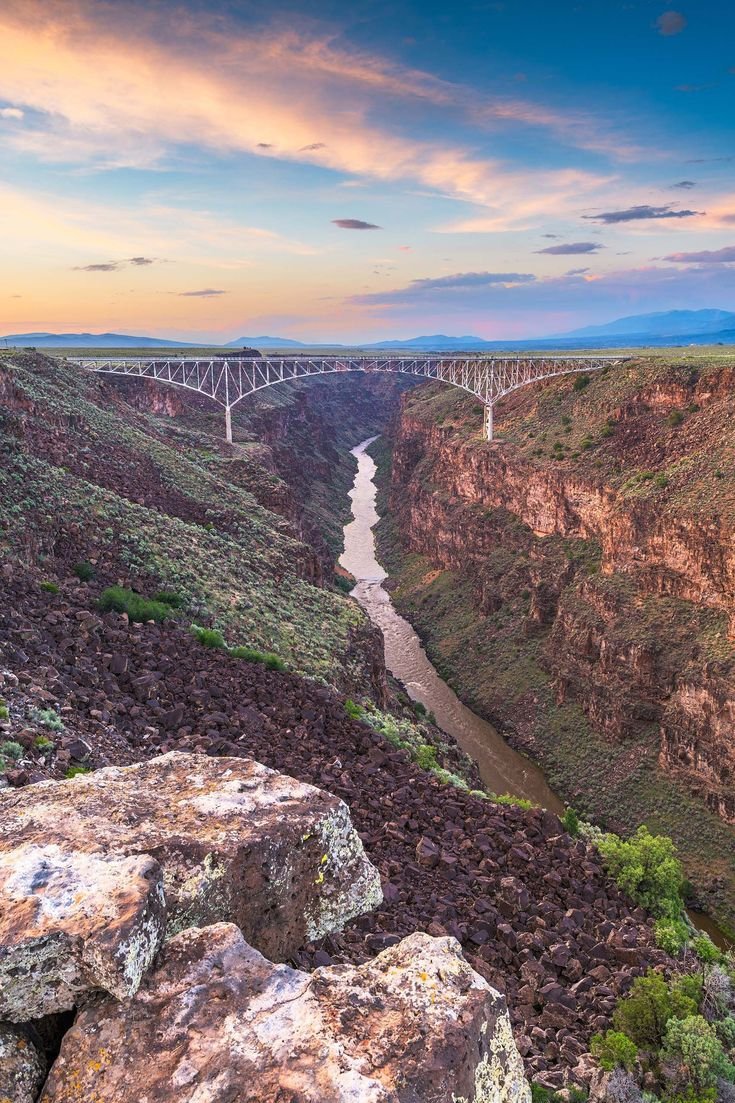 This may contain: a bridge over a river in the middle of a canyon