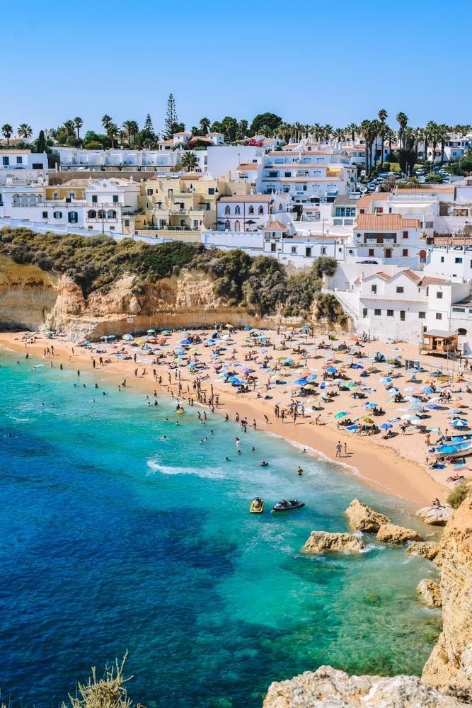 This may contain: the beach is crowded with people and umbrellas in clear blue water, surrounded by white buildings