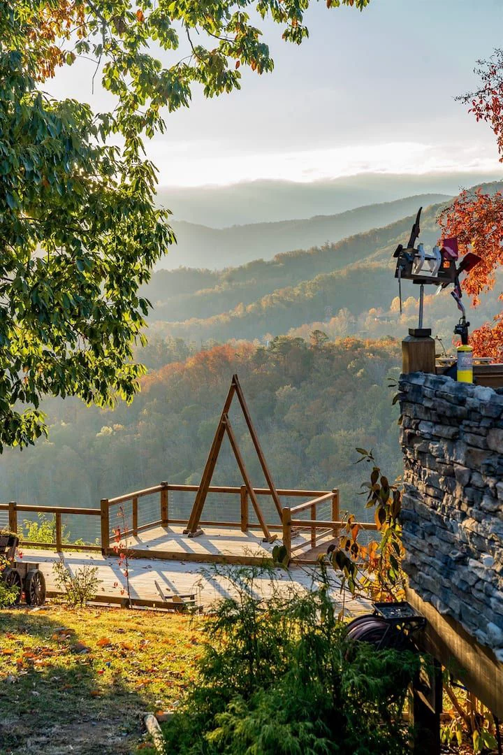 This may contain: a wooden bridge over a river surrounded by mountains in the distance with trees and foliage